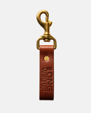 The Long Way Shops Long Way Up Lanyard features a brown leather strap embossed with LONG WAY UP, a brass swivel clasp, and a gold rivet, all shown against a plain white background.