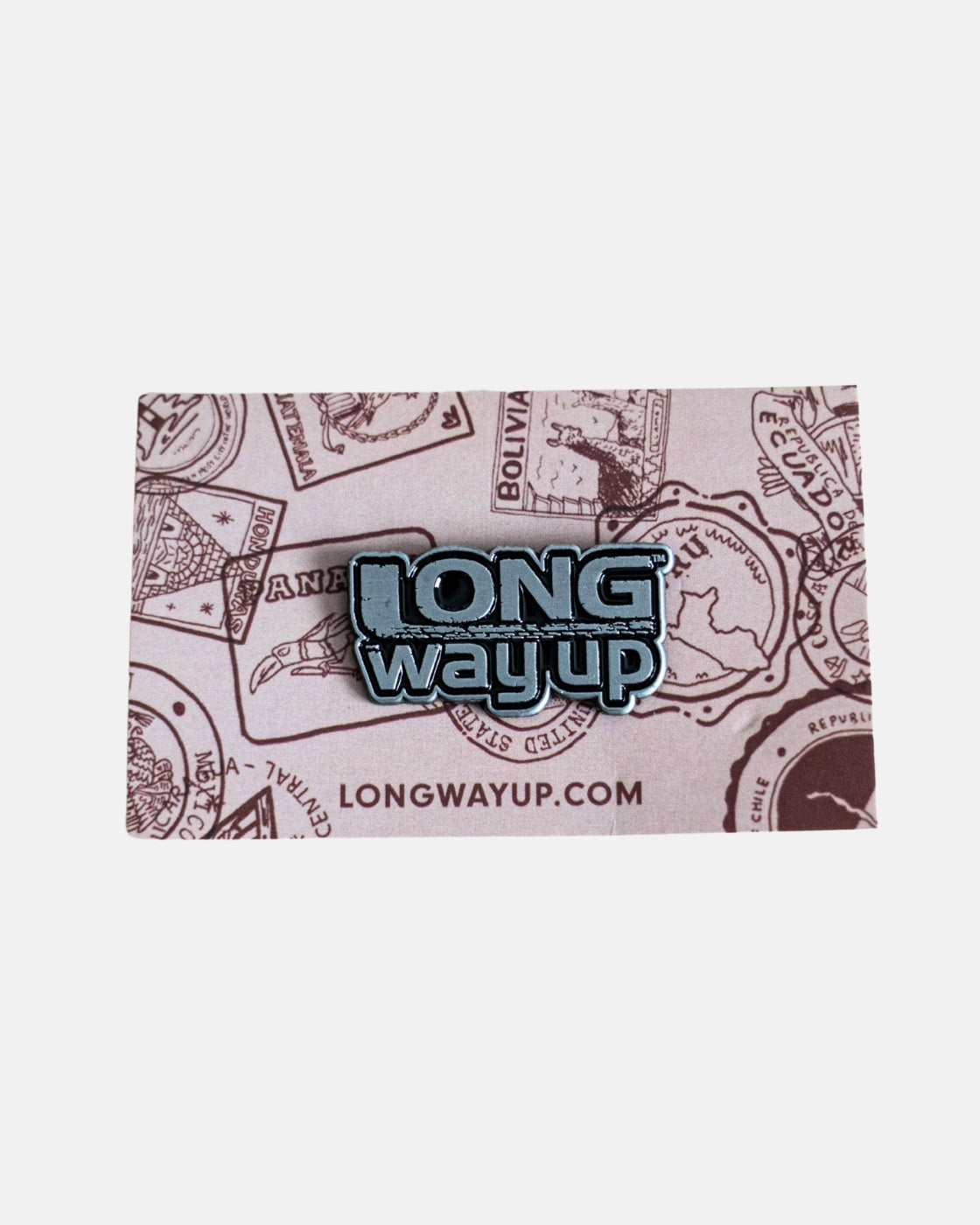 The Long Way Up Pin Badge by Long Way Shop features Long Way Up text, attached to a travel-themed card with illustrated passport stamps and the URL LONGWAYUP.COM at the bottom on a light background.