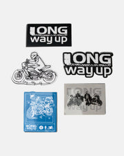 The Long Way Up Sticker Pack from Long Way Shop includes five stickers: two text-only designs, a motorcyclist line drawing, a blueprint-style motorcycle, and a transparent sticker featuring two riders on motorcycles.