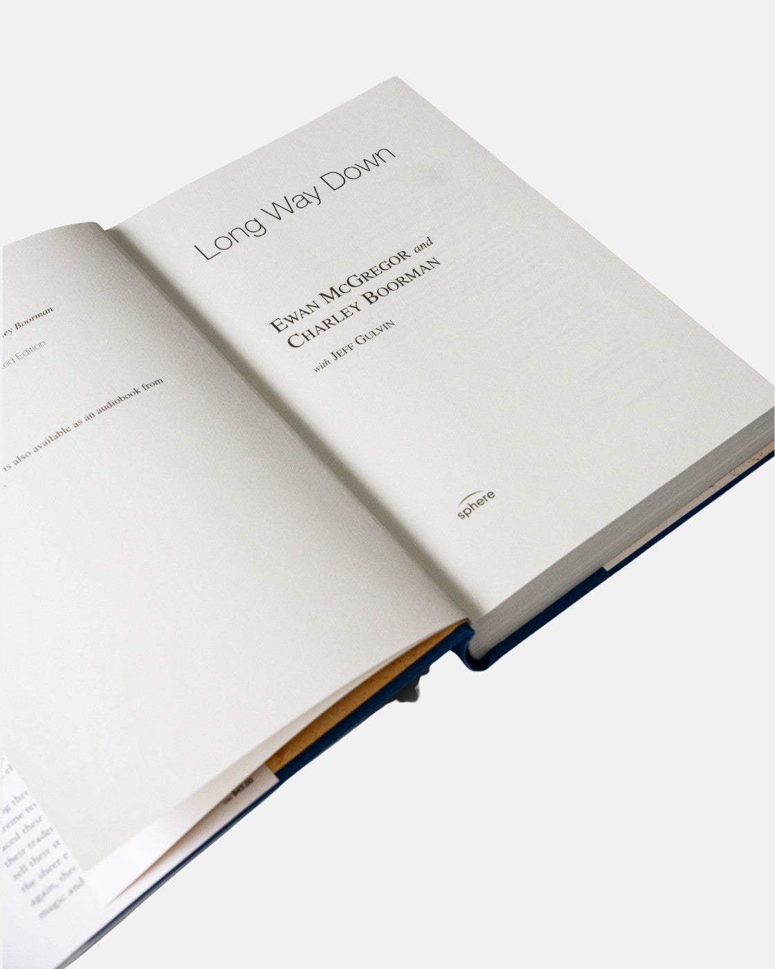 An open Long Way Down Book (Hardback) from Long Way Shop displays its bold black title on white pages, capturing the spirit of Ewan McGregor and Charley Boormans epic motorcycle adventure against a plain background.