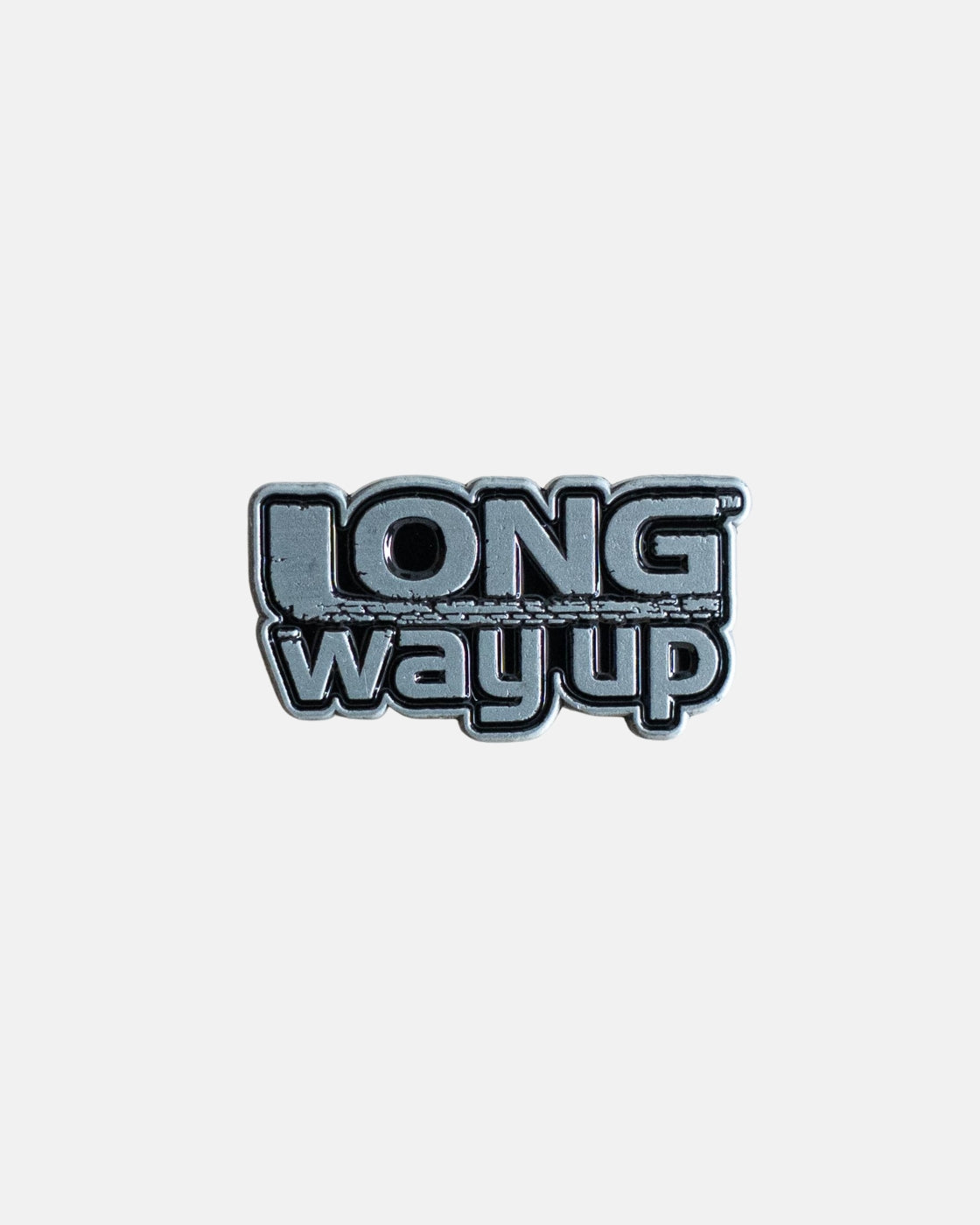 The Long Way Shops Long Way Up Pin Badge features bold, stylized text reading LONG way up on a sleek metallic pin, set against a plain light gray background.