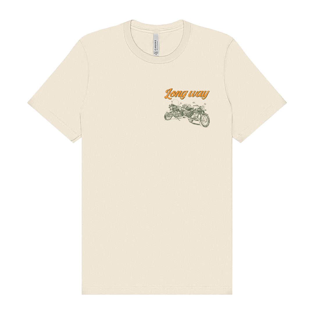 The Long Way Shop’s Long Way Bike Mountain Natural T-Shirt is made from soft Airlume combed cotton in a natural beige tone. It features a vintage motorcycle graphic on the upper left chest, with the words “Long way” in orange cursive above the bike. This unisex tee uses DTG printing and offers a tailored fit for comfortable, everyday style.